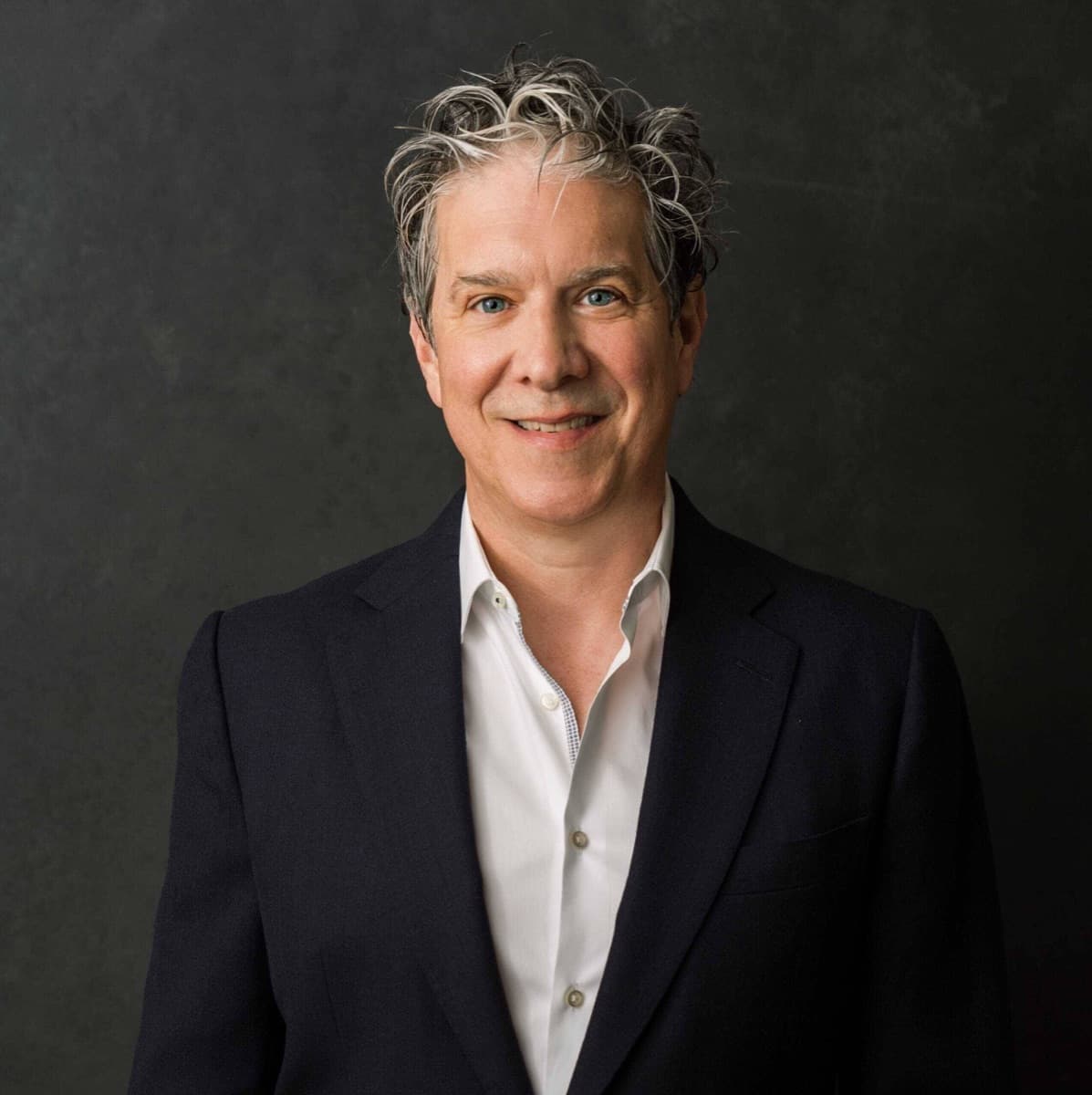 Portrait of a smiling man with grey curly hair in a dark jacket