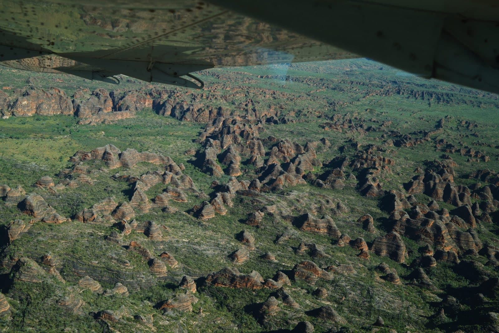 An aerial view of banded rock domes in a green landscape, seen from a plane wing