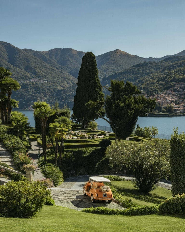 Cypress trees in a garden above a lake with mountains behind